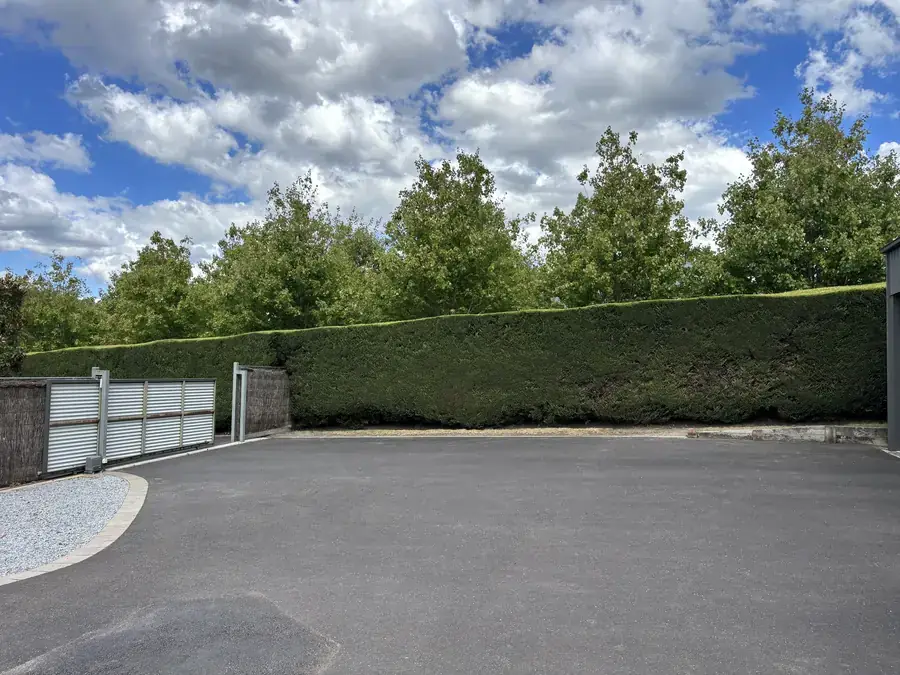 Tall driveway screening hedge trimmed back clear of the entry gate