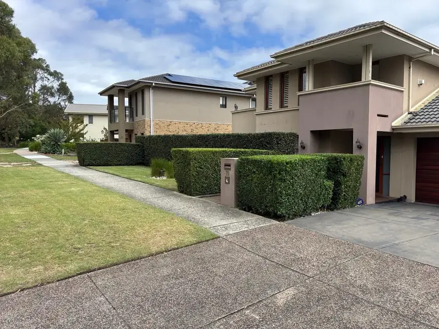 Shaped hedges lining the driveway of a two-storey home after trimming