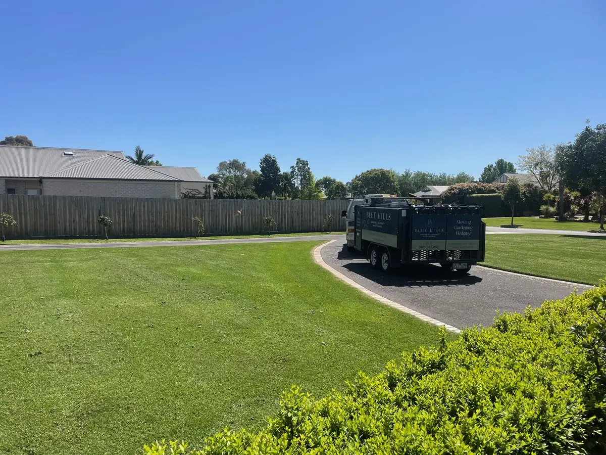 Wide residential lawn mowed and edged by Blue Hills, with the branded trailer on the driveway